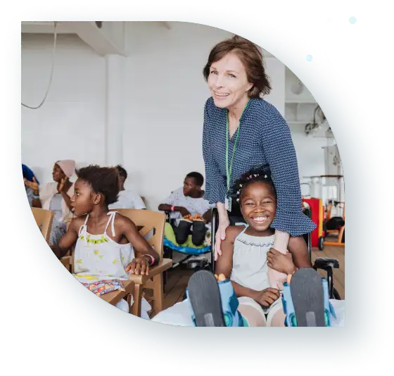 Smiling woman hugging a child in a classroom filled with other children