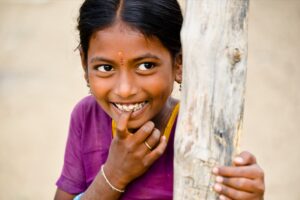 Smiling girl hiding behind a tree biting her finger